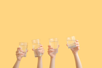 Women holding glasses with clean water on yellow background