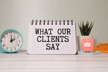 What Our Clients Say statement on paper note pad. Office desk with electronic devices and computer,