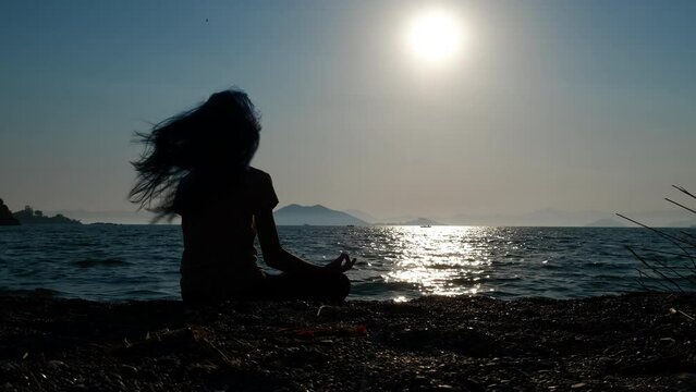 Girl practising proper breathing. A nice silhouette of young girl practising breathing exercices on the empty bay by the calm sea waves during evening time.