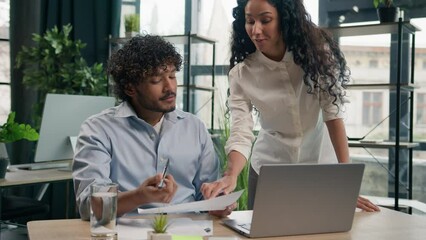 Hispanic woman leader mentor business coach help Arabian man intern with corporate laptop work at office businesswoman teach businessman explain financial paperwork new employee adaptation assistance