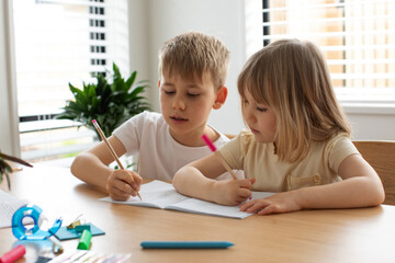 Brother and sister write and draw together with pencils at the table. The concept of home schooling
