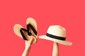 Female hands with wicker hat and flip flops on red background - obrazy, fototapety, plakaty
