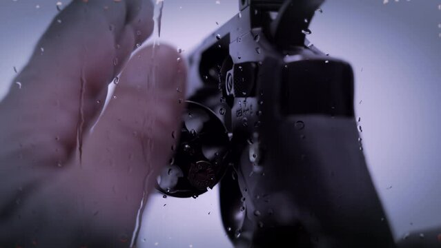 Russian Roulette slow motion of the rolling barrel of a revolver - water dripping through glass window in the foreground - on white background