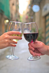 Elegant Toast: Close-up of Hands Holding Red and White Wine Glasses Making a Toast on a Peaceful Street - Vertical Format with Copyspace