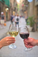 Elegant Toast: Close-up of Hands Holding Red and White Wine Glasses Making a Toast on a Peaceful Street - Vertical Format with Copyspace