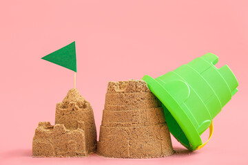 Castle made of sand with toy bucket and flag on pink background