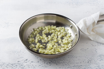 A frying pan with onions fried in butter on a light blue background. Cooking homemade risotto with pear and gorgonzola, step by step, step 2
