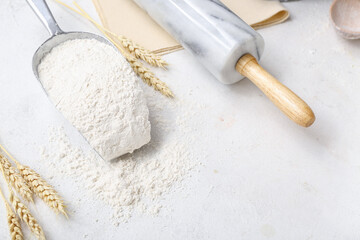 Fototapeta na wymiar Scoop with wheat flour and rolling pin on white background