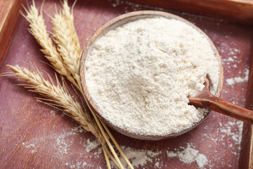 Bowl with wheat flour and spikelets on wooden tray, closeup