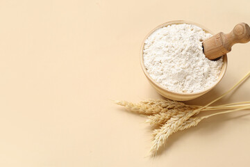 Bowl with wheat flour and scoop on beige background