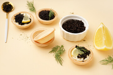 Tasty tartlets with black caviar on beige background