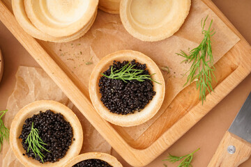 Wooden board of tasty tartlets with black caviar on beige background