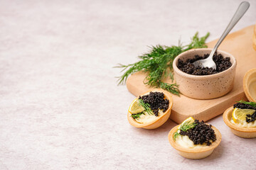 Tasty tartlets with black caviar on light background