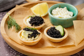 Plate of tasty tartlets with black caviar on grey background