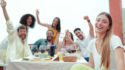 Group of happy people taking a selfie on a rooftop lunch party celebration, laughing together. Smiling woman looking at camera and enjoying a meal with her best friends on a friendly diner meeting