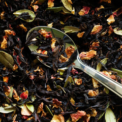 Teaspoon among black flavored tea with fruits, berries and flower petals. Macro. View from above. Photo