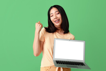 Happy young female Asian programmer with laptop on green background