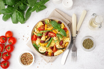 Bowl of tasty pasta salad with tomatoes and basil on white background