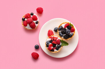 Plate of tasty tartlets with whipped cream and berries on pink background