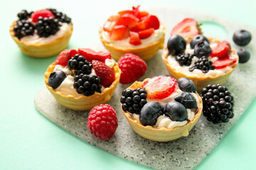 Board of tasty tartlets with whipped cream and berries on turquoise background