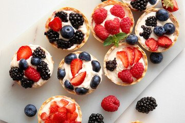 Board of tasty tartlets with whipped cream and berries on beige background