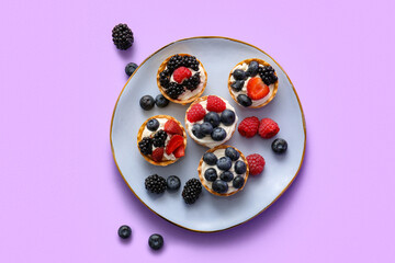 Plate of tasty tartlets with whipped cream and berries on lilac background
