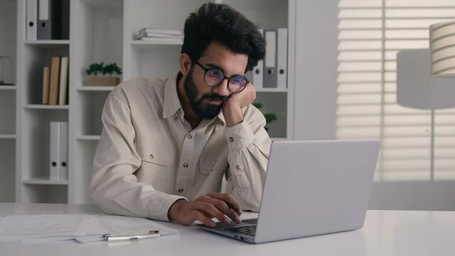 Tired Arabian muslim man overworked laptop remote job drowsy exhausted lazy Indian businessman ceo executive manager low energy monotone boring paperwork write business notes asleep overwork in office
