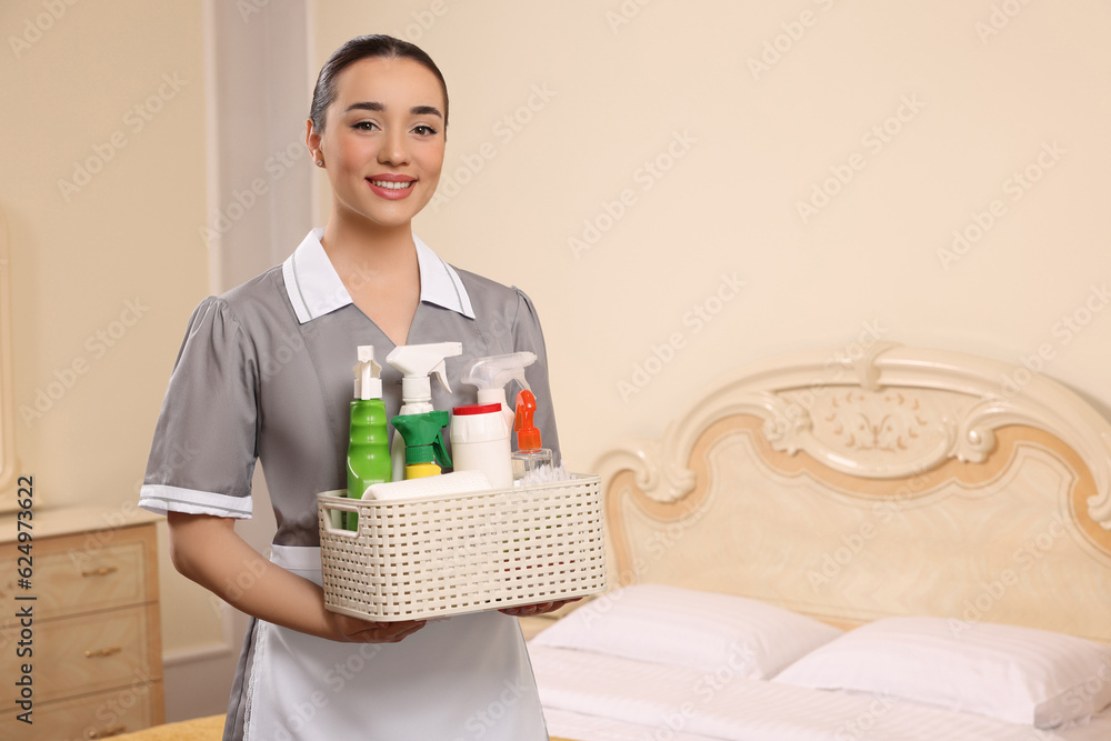 Canvas Prints Young chambermaid holding basket with cleaning products in hotel room. Space for text