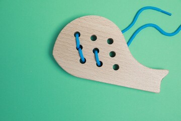 Wooden whale figure with holes and lace on green background, top view. Educational toy for motor skills development