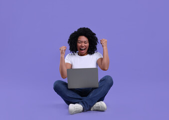 Emotional young woman using laptop on purple background