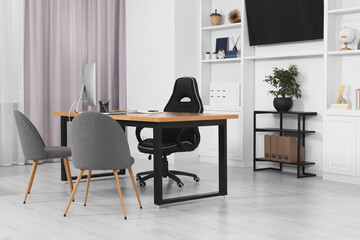 Stylish director's workplace with wooden table, tv zone, shelves and comfortable armchairs in room. Interior design