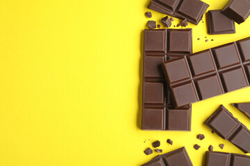 Pieces of delicious dark chocolate bars on yellow background, flat lay. Space for text