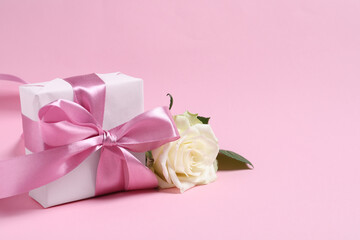 Gift box and beautiful rose flower on pink background, space for text