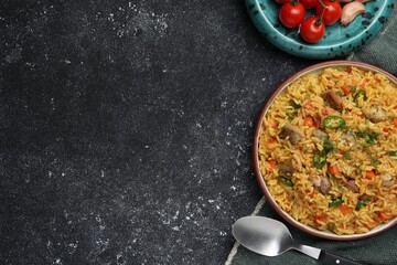 Delicious pilaf with meat and ingredients on black textured table, flat lay. Space for text