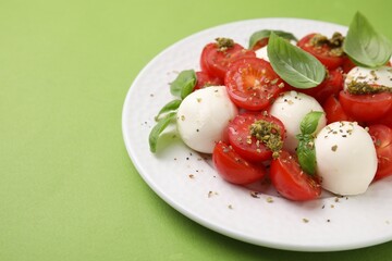 Tasty salad Caprese with tomatoes, mozzarella balls and basil on green background, closeup. Space for text
