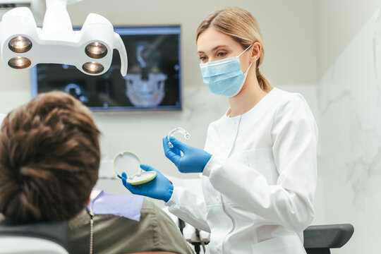 Portrait of friendly female dentist, orthodontist  in protective face mask showing aligners to patient. Dental, health care, teeth protection concept