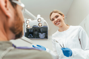 Portrait of smiling professional dentist talking with patient in modern dental clinic. Health care, oral hygiene concept 	