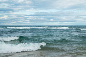 Fototapeta na wymiar Vastidão do oceano com ondas no litoral do Brasil em uma tarde com nuvens. 