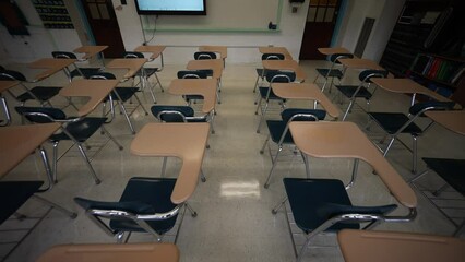High camera looking down pushes forward through a row of empty desks chairs with smart board, whiteboard, marker board.
