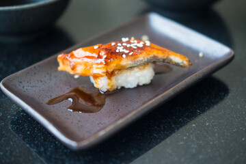 Eel fish grilled on rice moisten with sweet sauce and white sesame in black plate. Sushi menu. Japanese food.