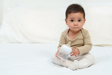 baby drinking water from bottle on bed