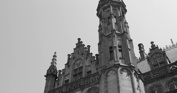 Grayscale Shot Of Gothic Tower Of The Historium Building During Daytime In Bruges, Belgium. low-angle