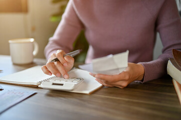 A woman sitting at a table using a calculator, and planning her household expenses.