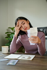 A stressed Asian woman worried about her monthly expenses while checking her electric bills