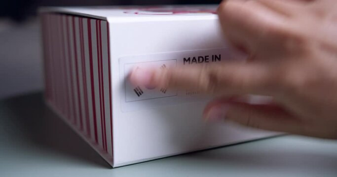 Hands applying MADE IN KOREA flag label on a shipping cardboard box with products. Close up shot with premium quality barcode.