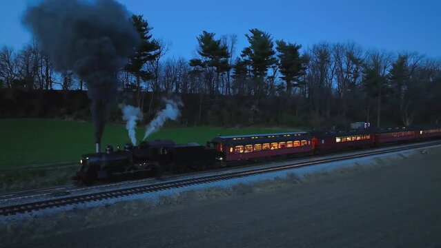 Drone Slightly Ahead and Parallel Night View of a Steam Passenger Train Stopped Blowing of Smoke