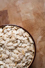 nigerian egusi seeds in a brown bowl on a wood surface, shelled melon seeds in a ceramic bowl, nigerian melon seeds, pumpkin seeds for cooking