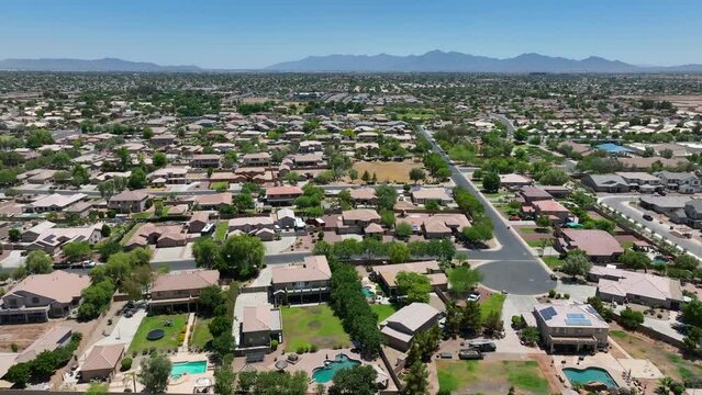 Upscale neighborhood with mountain range in distance. Many houses with pools and solar panels in desert climate. Southwestern USA housing development. Population growth theme. Aerial truck shot.
