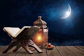 Muslim lantern with old Quran book on table at night