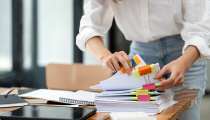 Closeup woman hand working in Stacks of paper files for searching and checking unfinished document...